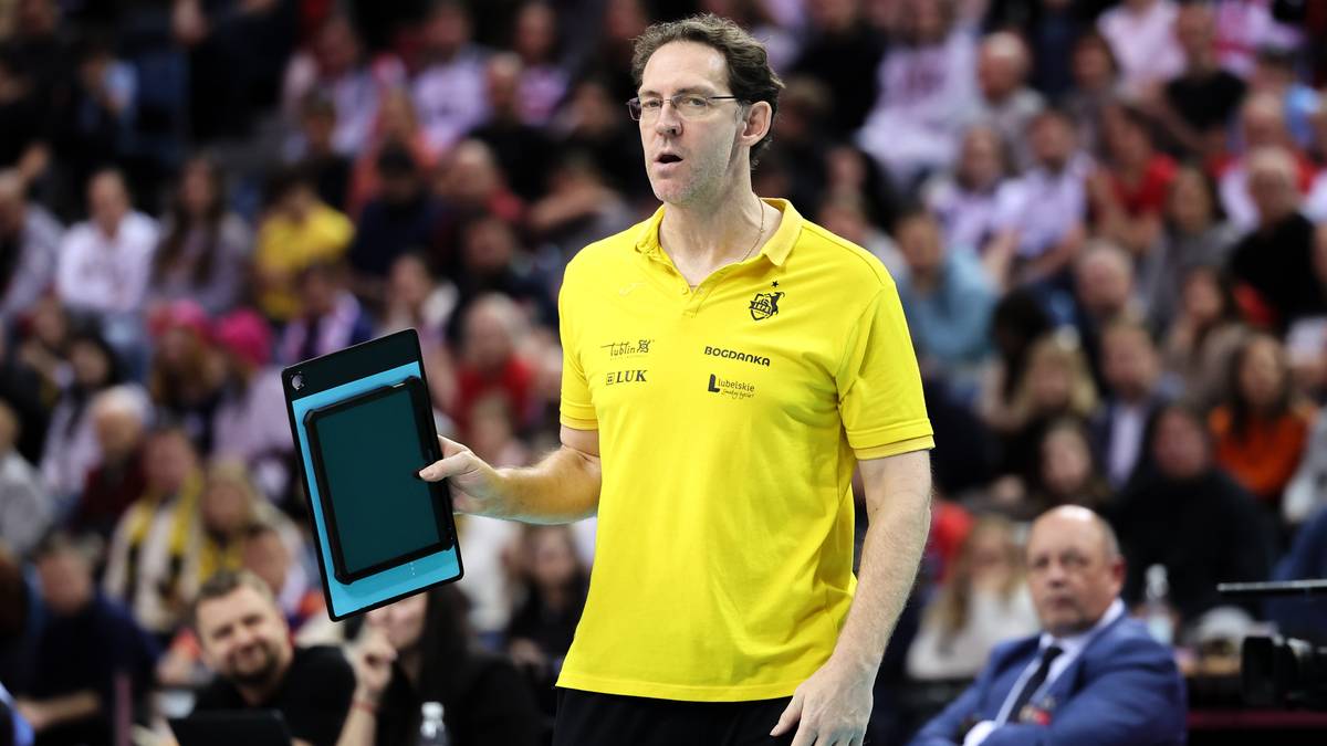 Trener siatkarski w ż&oacute;łtej koszulce z notesem w dłoni.