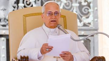 Papież Leon XIV przemawia do wiernych siedząc na krześle, trzymając w rękach kartki z tekstem i m&oacute;wiąc do mikrofonu.