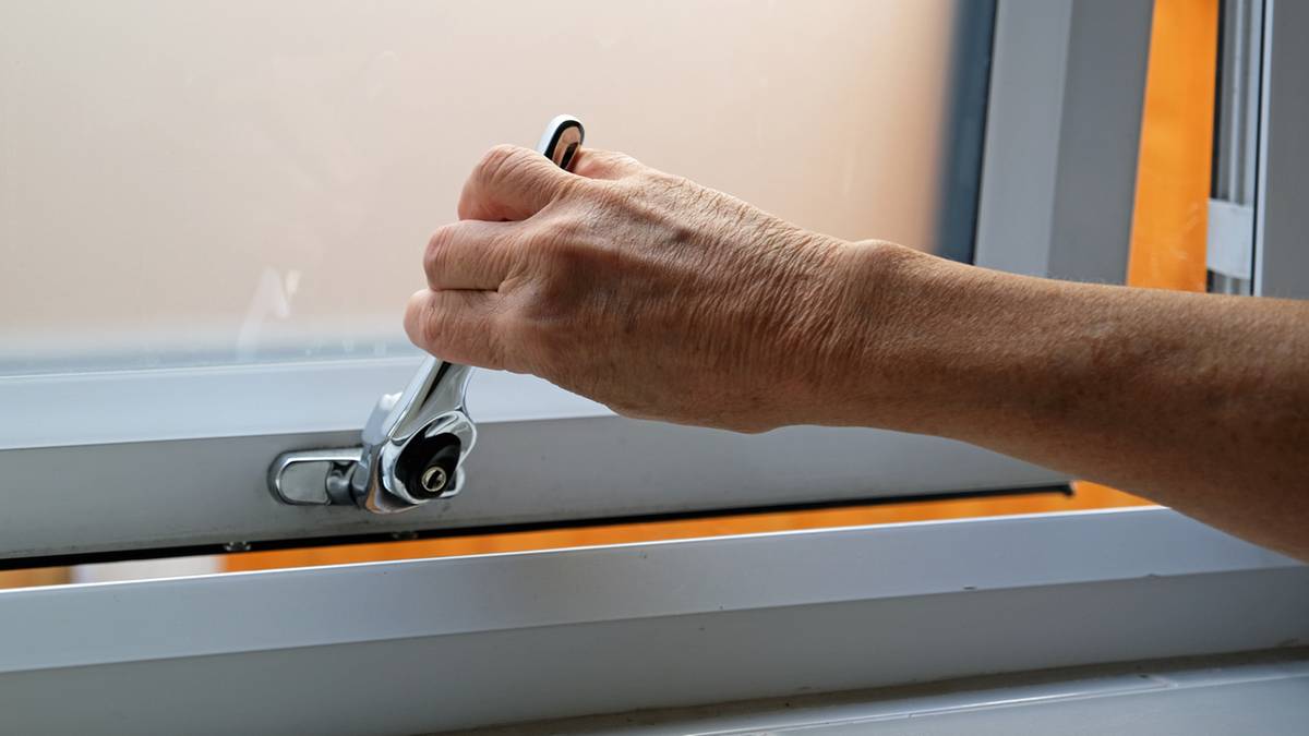 Dłoń przekręca klamkę okna, aby je uchylić.
