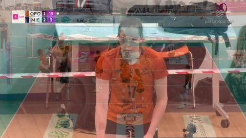 Siatkarka w pomarańczowej koszulce stoi na boisku do siatk&oacute;wki, patrząc w obiektyw. W tle widoczna jest tablica wynik&oacute;w pokazująca "OPO 1-13 MIE 2-0".