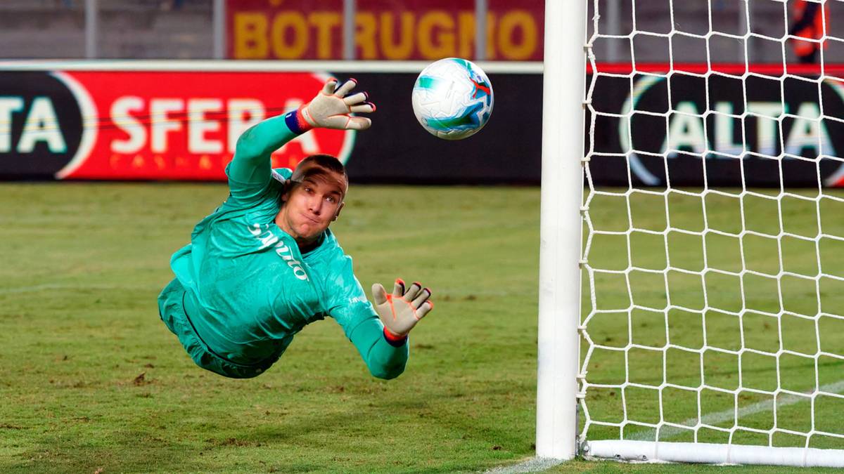 Bramkarz w zielonej koszulce wykonuje akrobatyczny rzut, próbując złapać piłkę w powietrzu.