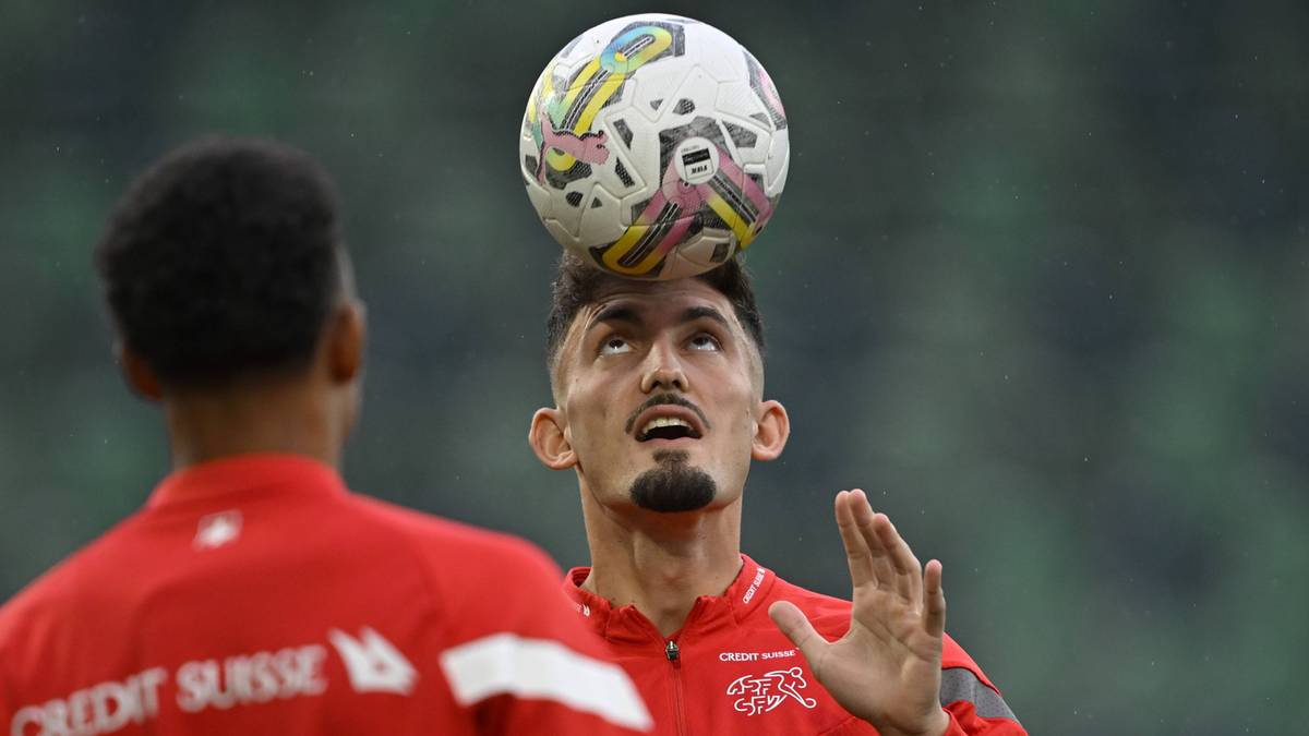 Piłkarz w czerwonej koszulce z piłką na głowie, patrzący w górę.