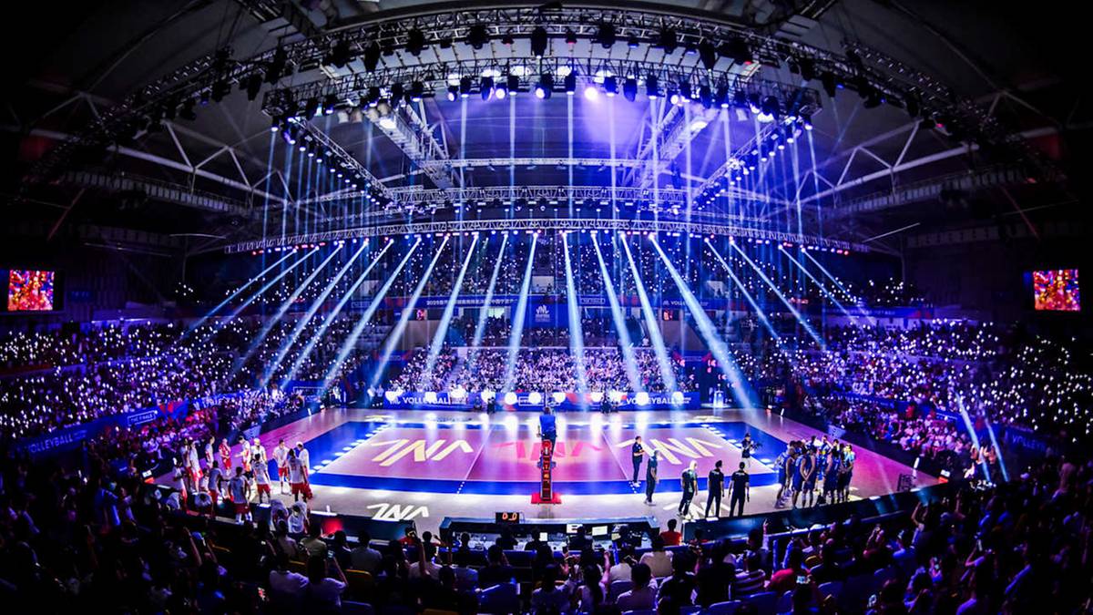 Widok z góry na pełną hali widowiskowej podczas meczu siatkówki, z zawodnikami na boisku i tłumem kibiców na trybunach. Efektowne oświetlenie sceniczne podkreśla atmosferę wydarzenia.