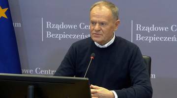 Premier Donald Tusk siedzi przy stole, przemawiając do mikrofonu. W tle widoczne napisy "Rządowe Centrum Bezpieczeństwa".