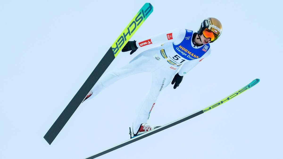 Skoczek narciarski w kombinezonie i z nartami podczas lotu.