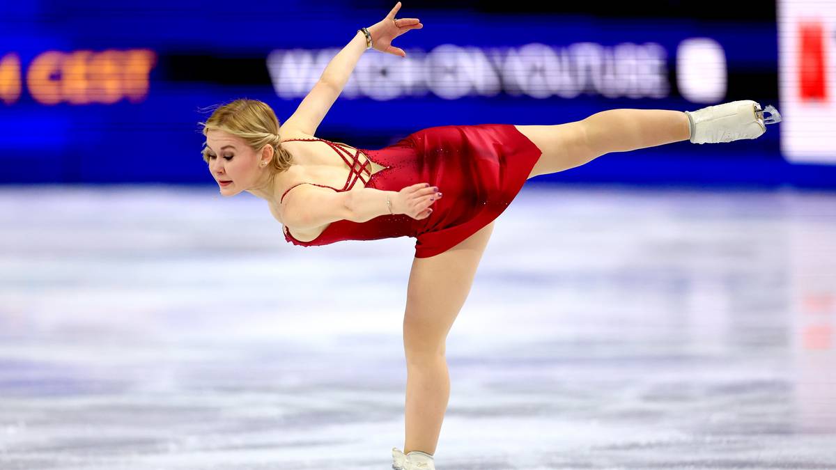 Łyżwiarka figurowa w czerwonej sukience wykonuje pozycję na lodzie.