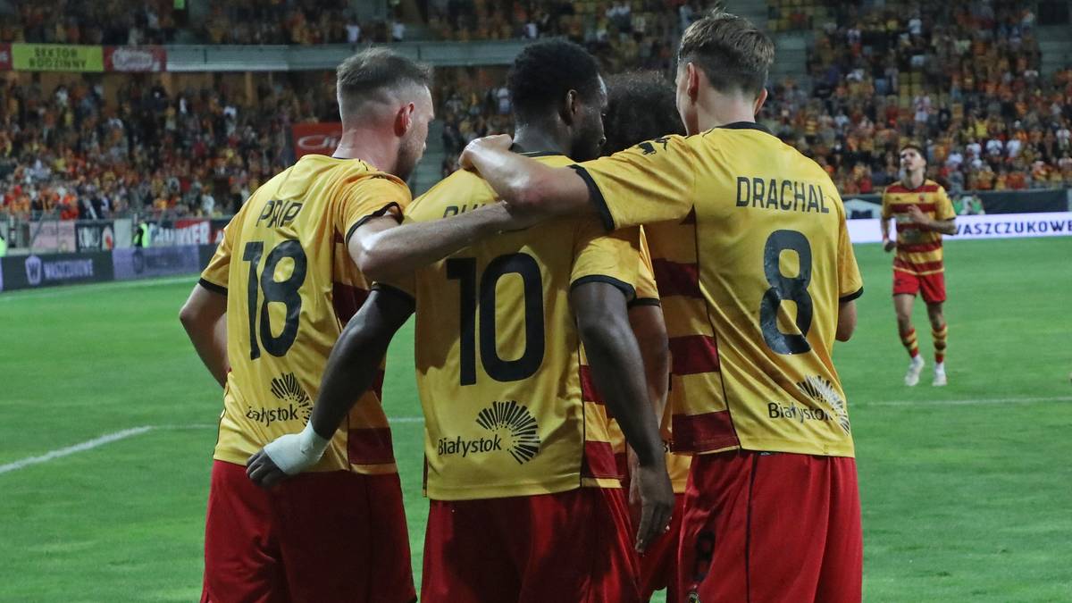 Czterech piłkarzy w żółtych koszulkach i czerwonych spodenkach obejmuje się w geście radości na boisku.