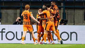 Grupa piłkarzy w pomarańczowych strojach świętuje gola na boisku.