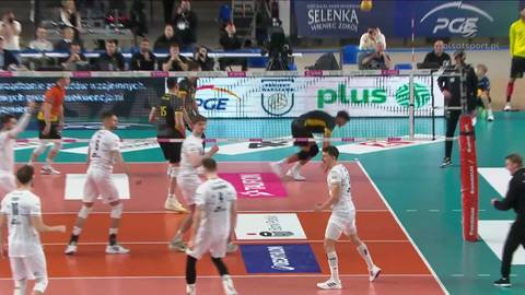 Siatkarz wykonujący zagrywkę serwisową, piłka leci w powietrzu, przeciwnicy reagują.