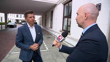 Ryszard Petru udziela wywiadu dziennikarzowi na zewnątrz budynku. Polityk stoi przed mikrofonem, ubrany w marynarkę i koszulę.