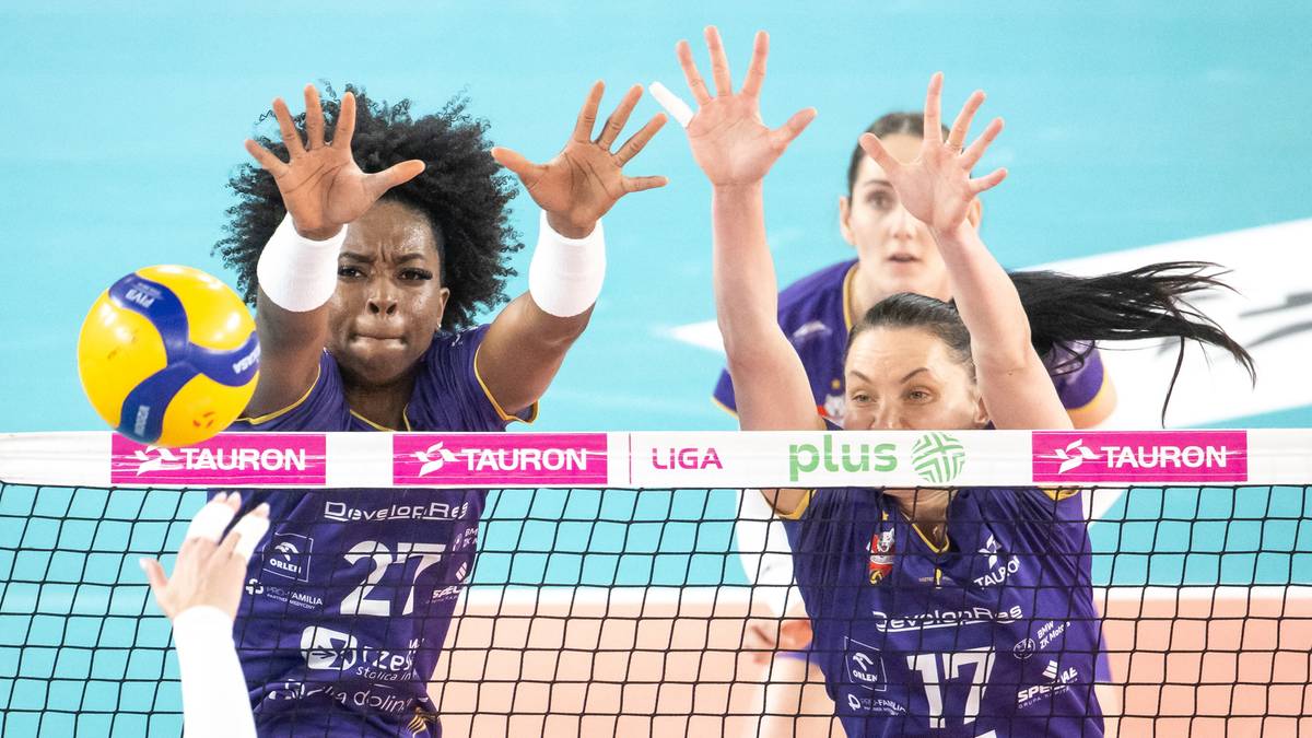 Siatkarka w granatowym stroju z numerem 27 blokuje piłkę przy siatce.