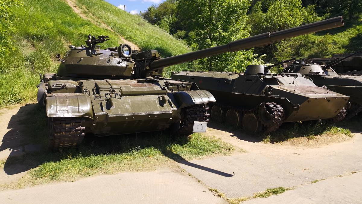 Kilka starych czołgów i pojazdów opancerzonych w kolorze zielonym, stojących na trawiastym podłożu.