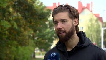Bartosz Bednorz udzielający wywiadu na tle zieleni i budynk&oacute;w