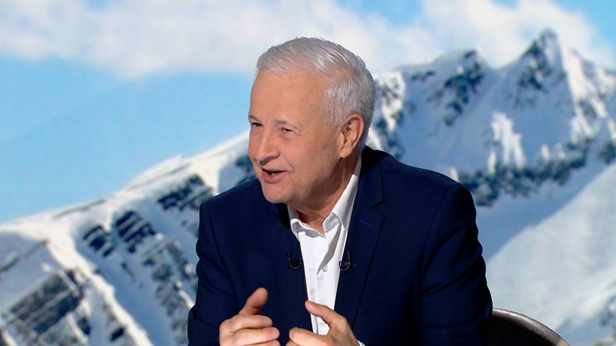 Apoloniusz Tajner, ubrany w białą koszulę i granatową marynarkę, m&oacute;wi, gestykulując rękami. W tle widoczne są ośnieżone g&oacute;ry pod błękitnym niebem.