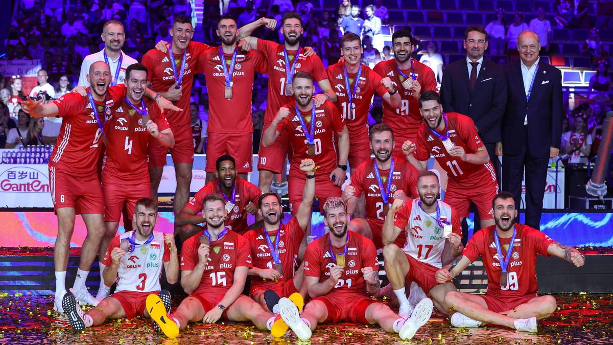 Drużyna siatkarska w czerwonych strojach pozuje do grupowego zdjęcia z pucharem, wyrażając radość i dumę po zwycięstwie.