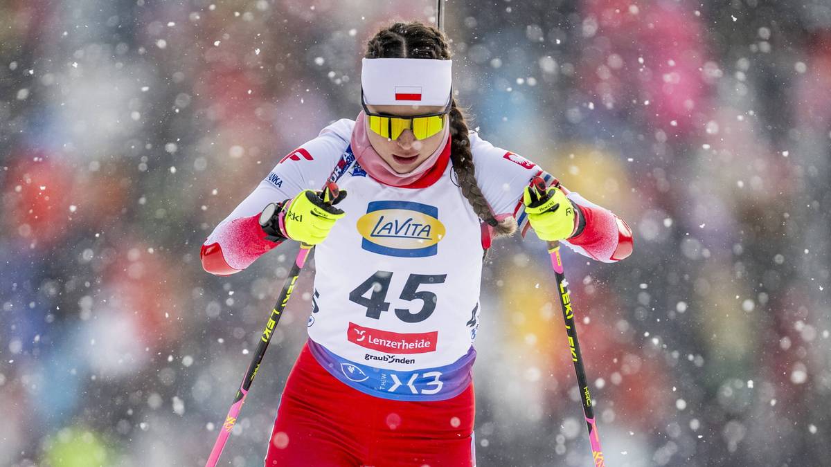 Biathlonistka w czerwonym stroju z białymi elementami i numerem startowym 45, stoi na śniegu podczas zawod&oacute;w w biatlonie, w tle widzowie na trybunach.