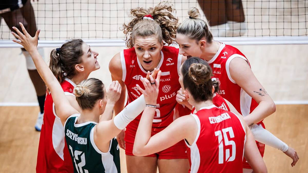 Grupa zawodniczek siatkówki w czerwonych strojach spiera się podczas przerwy na boisku.