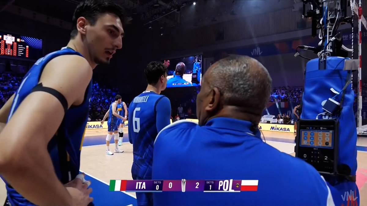 Siatkarze w niebieskich strojach podczas meczu siatkówki Polska - Włochy. Jeden z nich jest zwrócony bokiem do widza, patrząc w dal, a drugi stoi tyłem. Widoczny fragment wyniku na tablicy "ITA 0 0 2 POL".