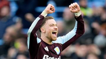 Piłkarz w bordowo-granatowej koszulce Aston Villi cieszy się z gola, unosząc ręce w górę.