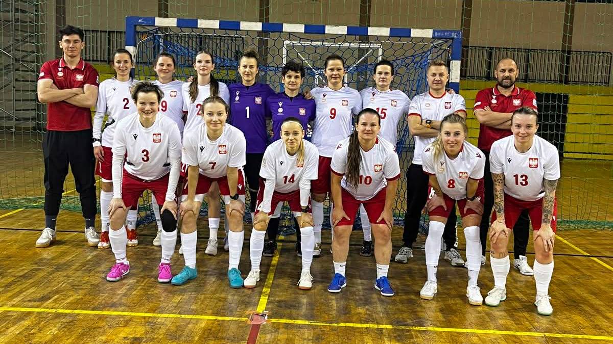 Drużyna piłkarska w komplecie pozuje do zdjęcia na parkiecie hali sportowej.