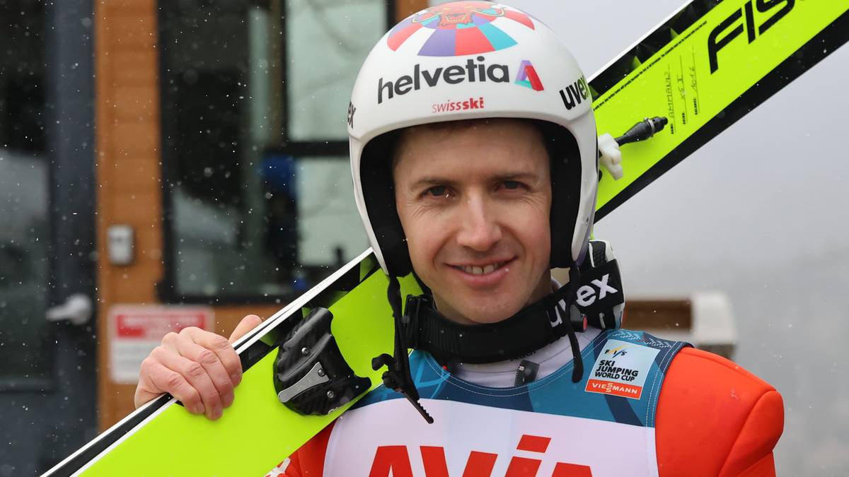 Simon Ammann, skoczek narciarski w stroju sportowym i kasku, trzymający narty.