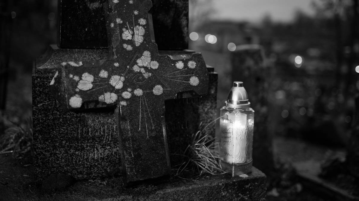 Kamienny krzyż nagrobny i zapalona znicz na cmentarzu, z rozmytym tłem.