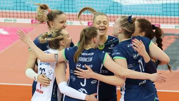 Grupa zawodniczek drużyny siatkarskiej w ciemnoniebieskich strojach sportowych, obejmująca się radośnie i śmiejąc się.