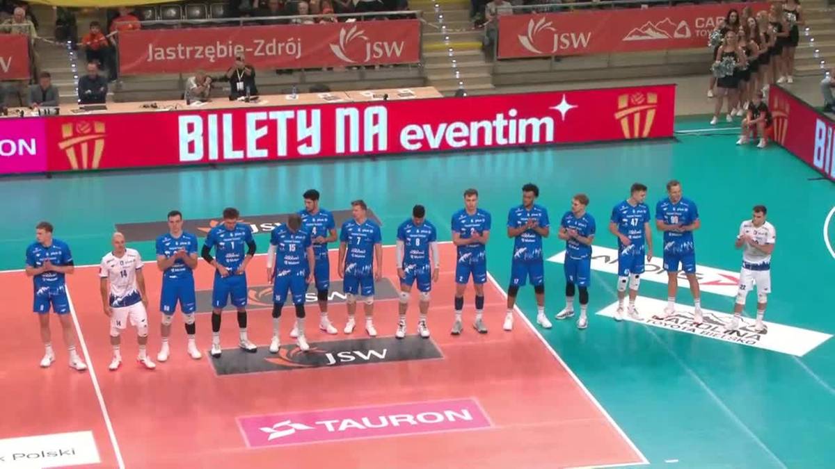 Drużyna siatkarzy w niebieskich strojach sportowych stoi na boisku do siatkówki.