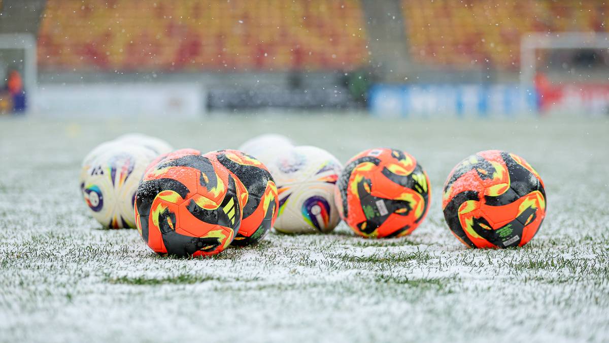 Piłki futbolowe leżące na zaśnieżonej murawie stadionu.
