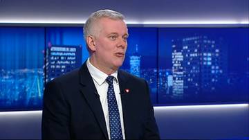 Mężczyzna w garniturze i krawacie m&oacute;wi w wywiadzie telewizyjnym.