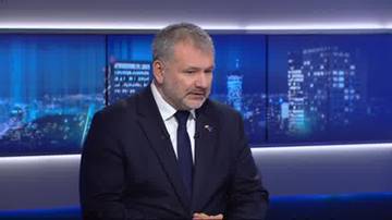 Waldemar Żurek w garniturze i krawacie siedzi w studiu telewizyjnym.