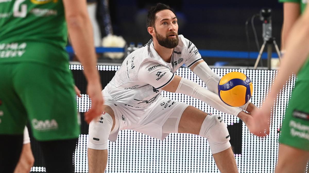 Siatkarz w białym stroju łapie piłkę do siatkówki podczas meczu.