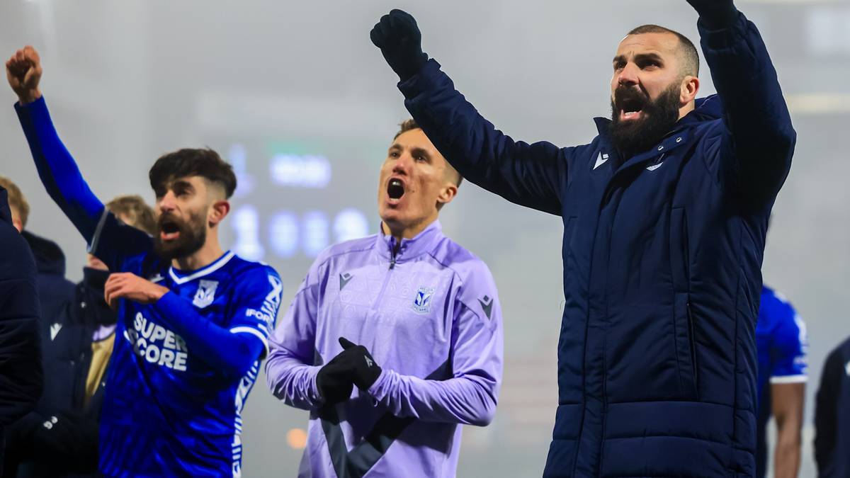 Trzech piłkarzy w piłkarskich strojach świętuje z podniesionymi rękami.