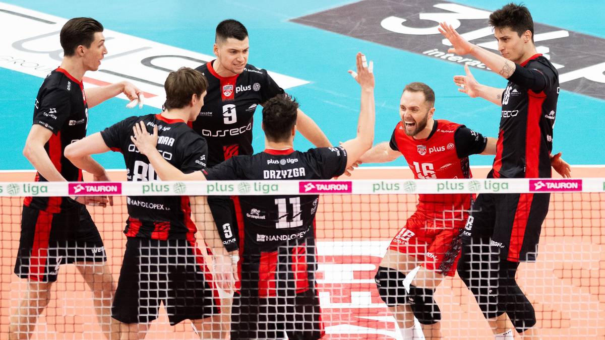 Siatkarze w czarno-czerwonych strojach świętujący na boisku siatkarskim.