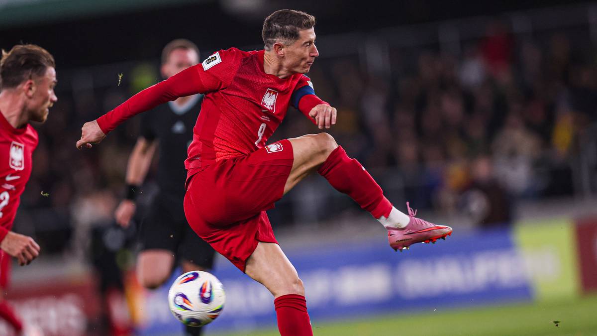 Piłkarz Robert Lewandowski w czerwonym stroju reprezentacji Polski kopie piłkę.