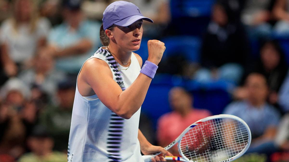 Iga Świątek unosi zaciśniętą pięść, trzymając rakietę tenisową, w tle widzowie na trybunach.