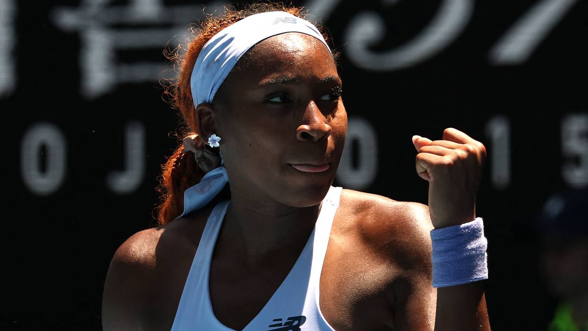 Coco Gauff, tenisistka, zaciśnięta pięść, biała opaska na głowie, niebieska opaska na nadgarstku, biała koszulka sportowa.