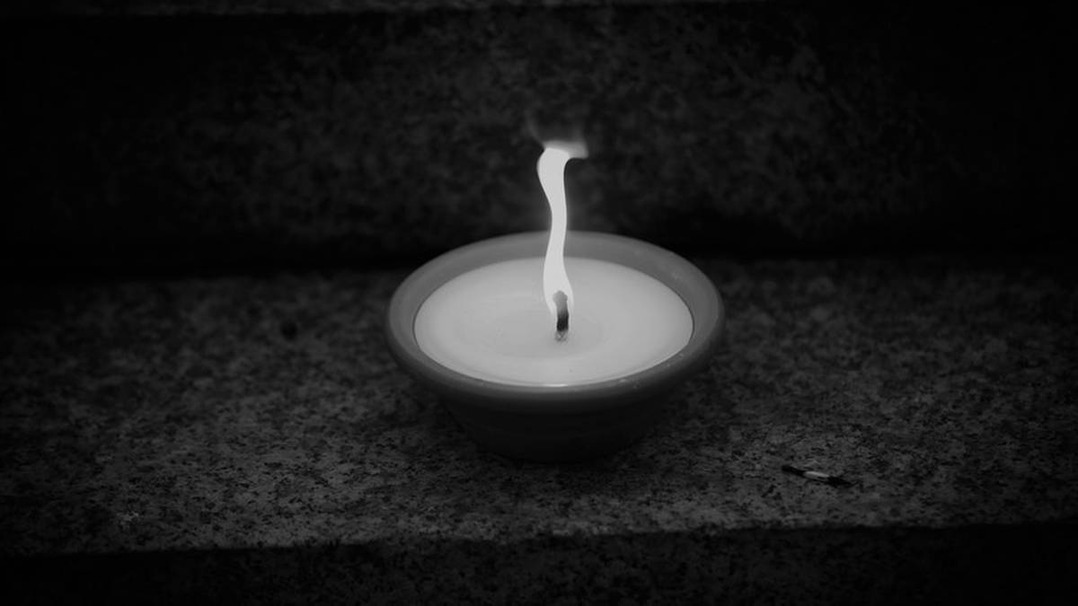 Płonąca biała świeca w ciemnym otoczeniu, symbol żałoby i pamięci.