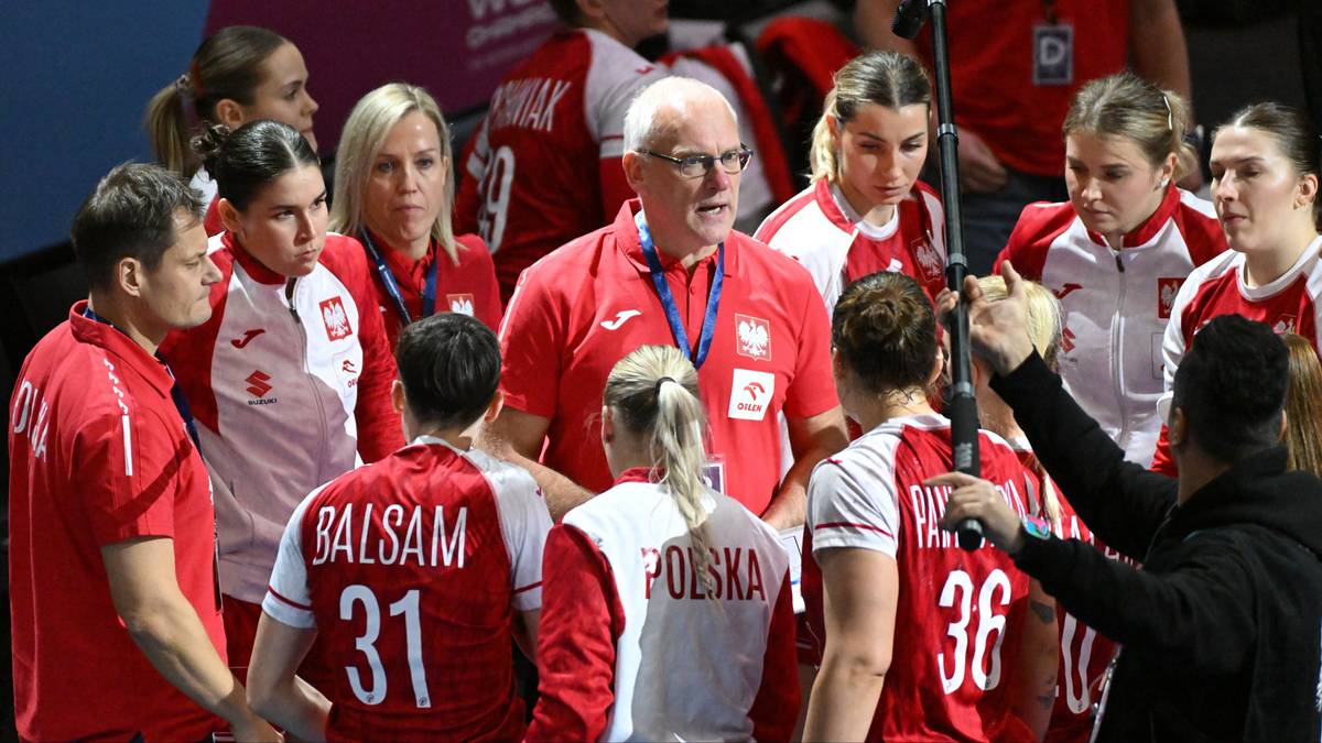 Trener w okularach i z siwą brodą przemawia do grupy zawodniczek w czerwonych strojach reprezentacji Polski, z widocznymi napisami "POLSKA" i numerami na koszulkach.