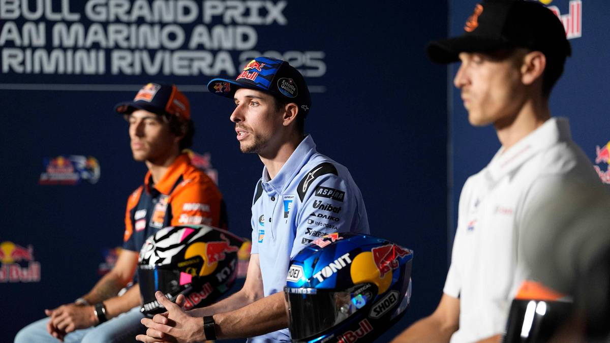 Trzech zawodników MotoGP siedzi w rzędzie, każdy z kaskiem na kolanach, podczas konferencji prasowej.