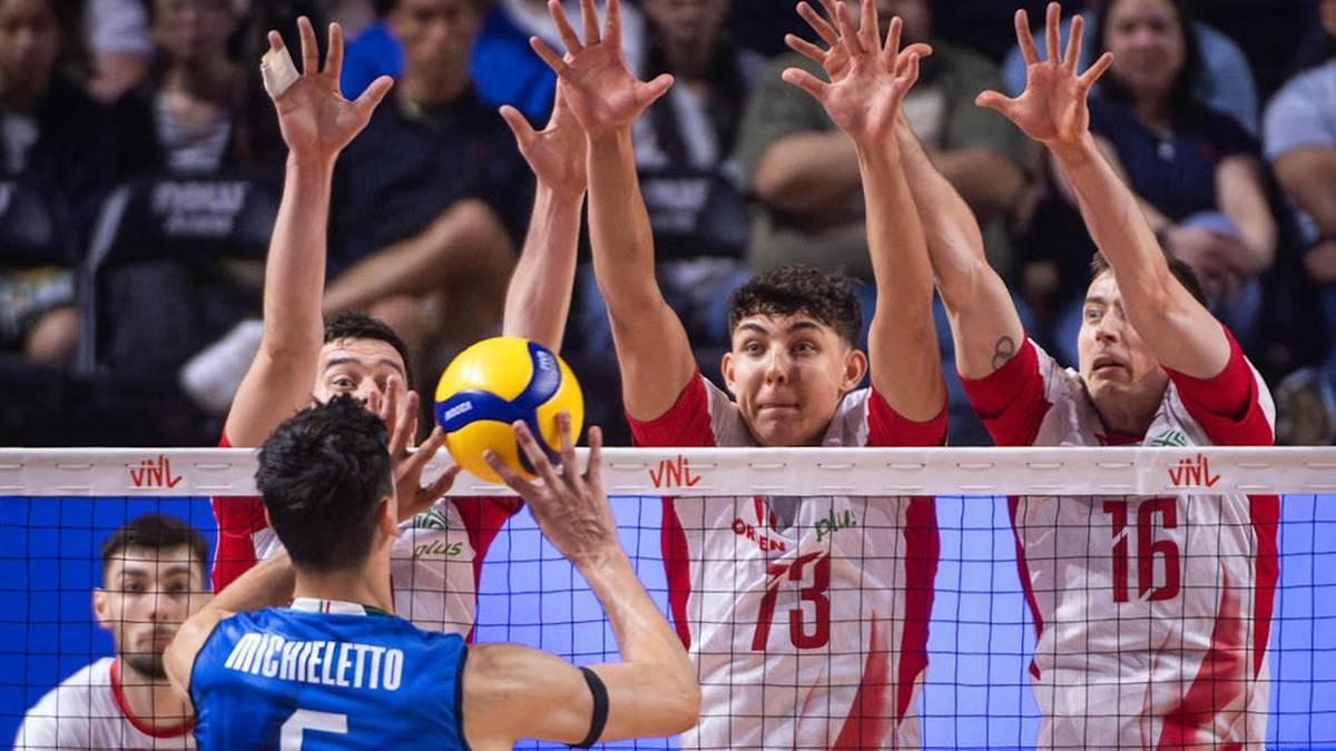 Siatkarze w białych i czerwonych strojach rozgrywają piłkę siatkową nad siatką. Jeden z zawodników łapie piłkę.