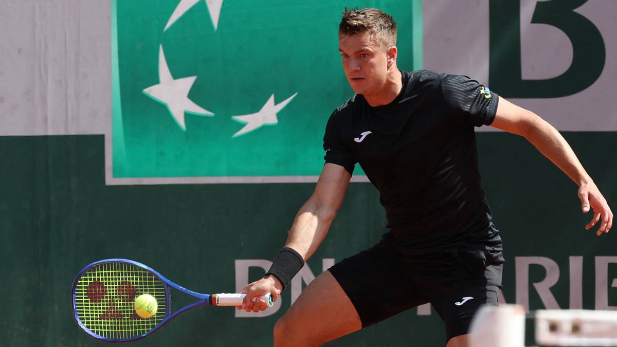 Gracz tenisa w czarnym stroju odbija piłkę rakietą na korcie ziemnym podczas US Open.