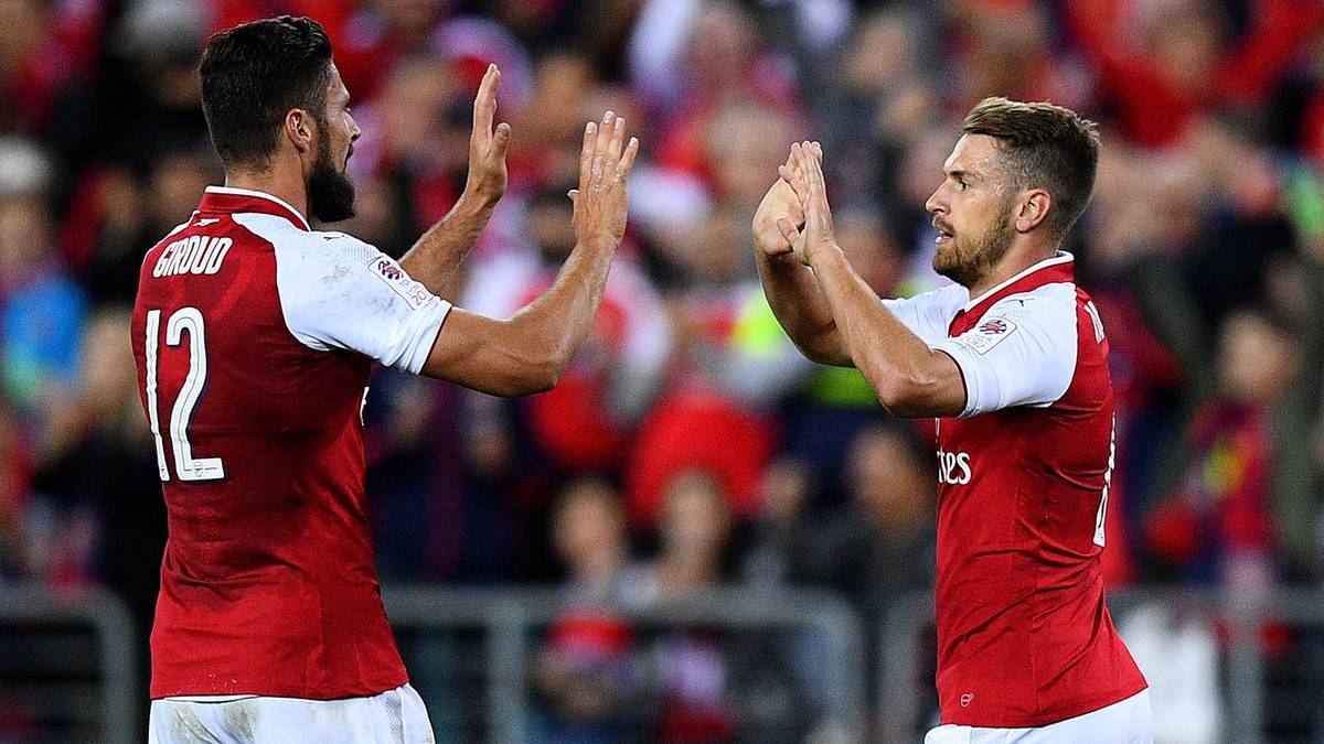 Trzech piłkarzy Arsenalu w czerwono-białych strojach świętuje na boisku.