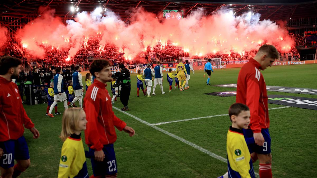 Piłkarze wychodzą na boisko stadionu w otoczeniu czerwonych rac odpalonych przez kibiców.