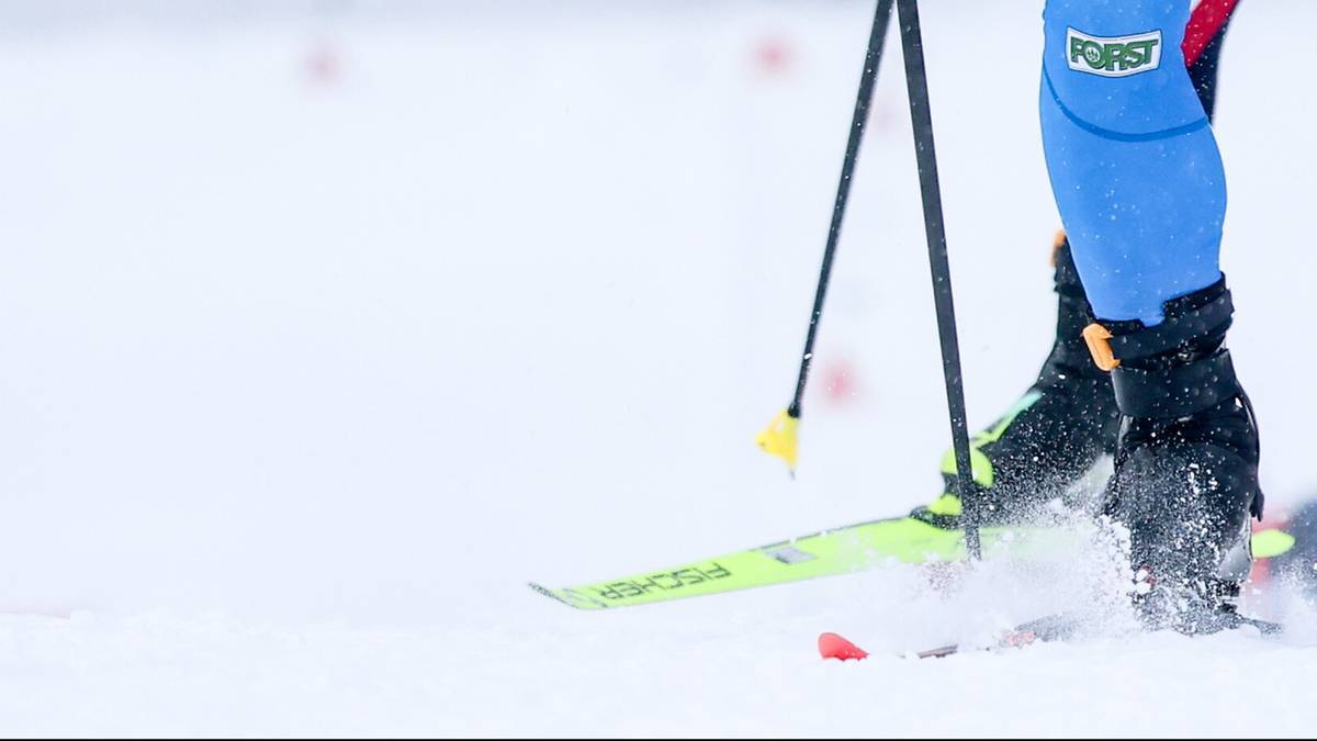 Biathlonistka w akcji na śniegu, widoczne narty, kijki i fragment stroju.