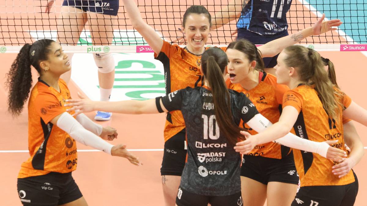 Grupa siatkarek w strojach sportowych cieszy się razem na boisku siatkarskim.