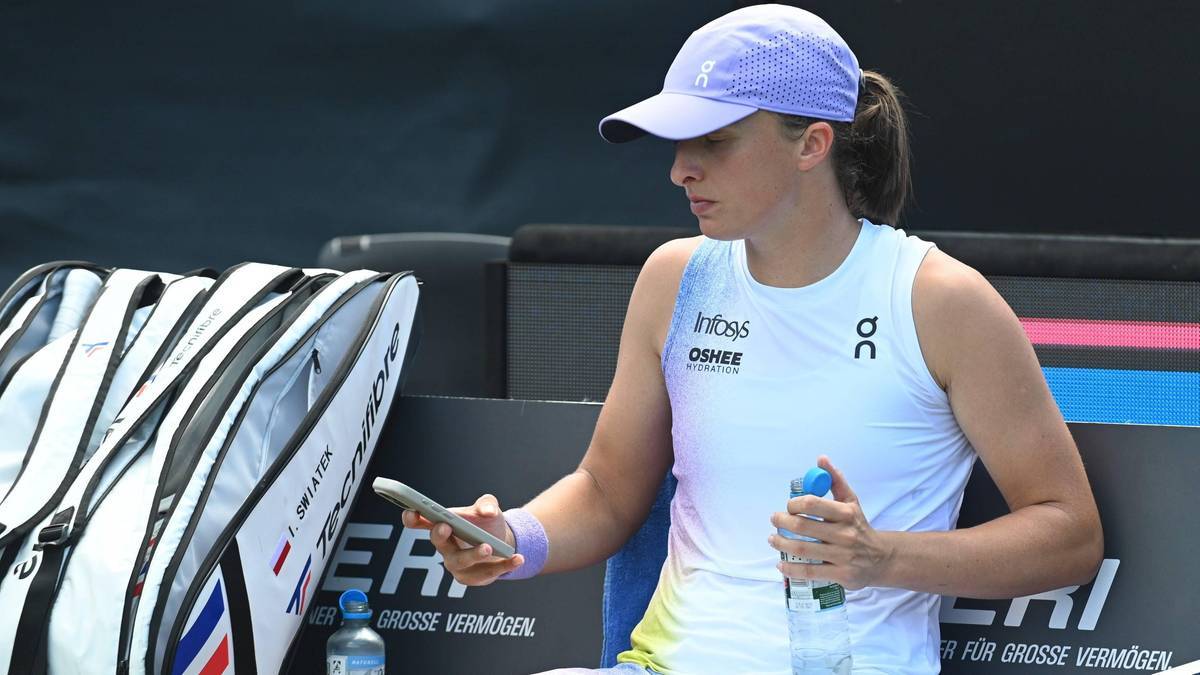 Iga Świątek w czapce z daszkiem i stroju tenisowym, trzymająca smartfon i bidon z napojem sportowym.
