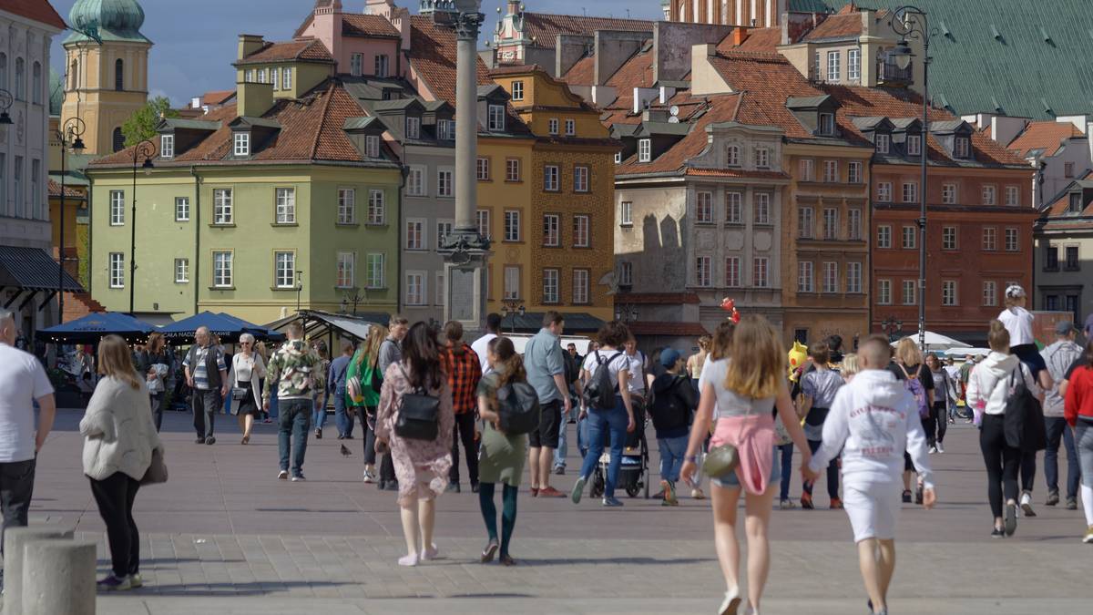 Ulica w mieście z grupami ludzi spacerujących przed kolorowymi budynkami.