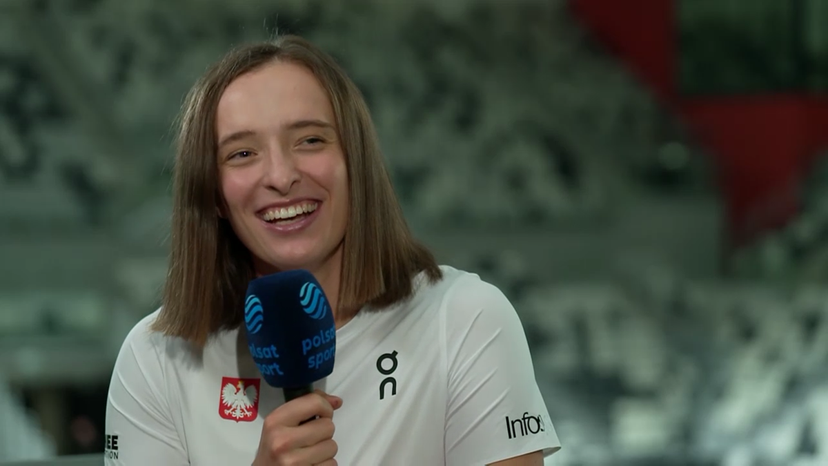 Iga Świątek udziela wywiadu, trzymając mikrofon Polsat Sport, ubrana w białą koszulkę reprezentacji Polski.