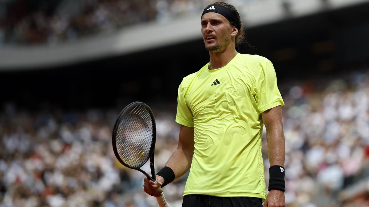 Tenisista w ż&oacute;łtej koszulce z czarną opaską na głowie trzyma rakietę tenisową podczas meczu na korcie ziemnym.